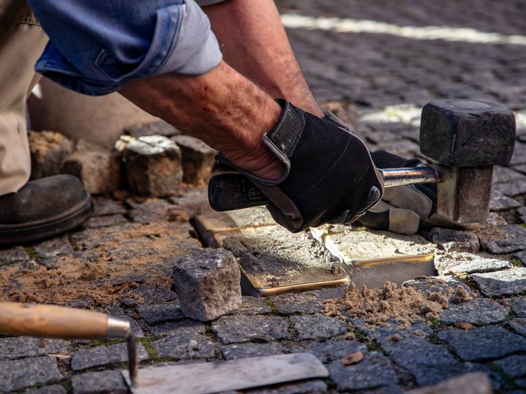 Blick auf Hände, die gerade Verlegearbeiten von Stolpersteinen erledigen.