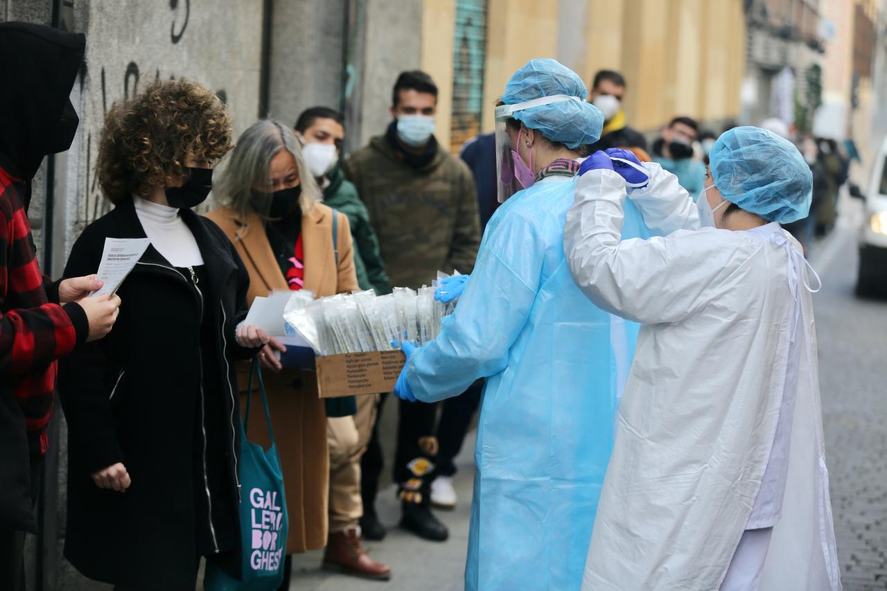 Eine Mitarbeiterin des Gesundheitswesens in Madrid hilft einer Kollegin beim Anziehen der Schutzkleidung, während sie Proben von Patienten nimmt, die vor einem öffentlichen Gesundheitszentrum auf einen Antigentest warten. 