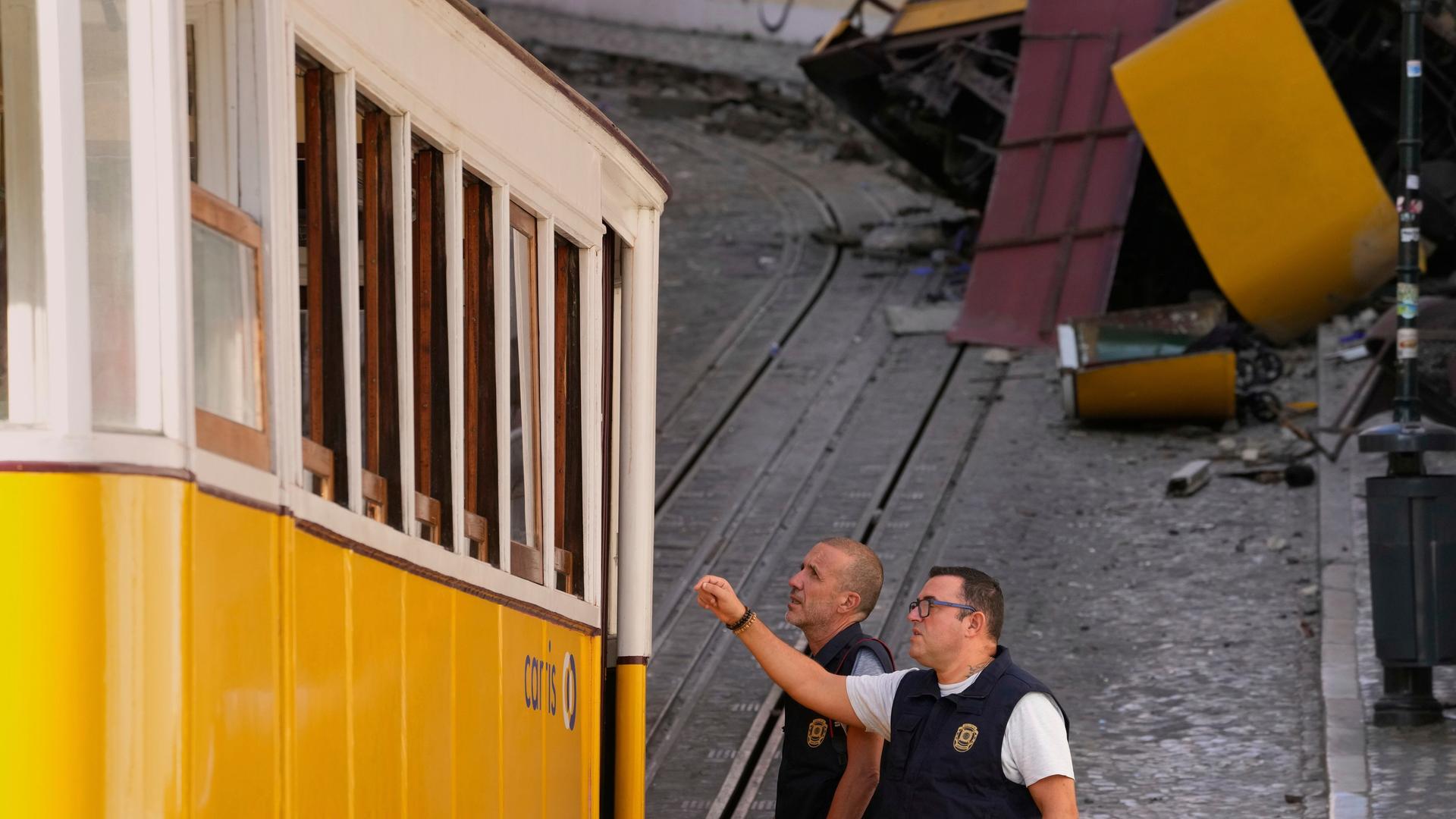 Zwei Polizeibeamte begutachten einen Waggon der Standseilbahn in Lissabon, dahinter ist der zerschellte Waggon zu sehen Zwei Polizeibeamte begutachten einen Waggon der Standseilbahn in Lissabon, dahinter ist der zerschellte Waggon zu sehen