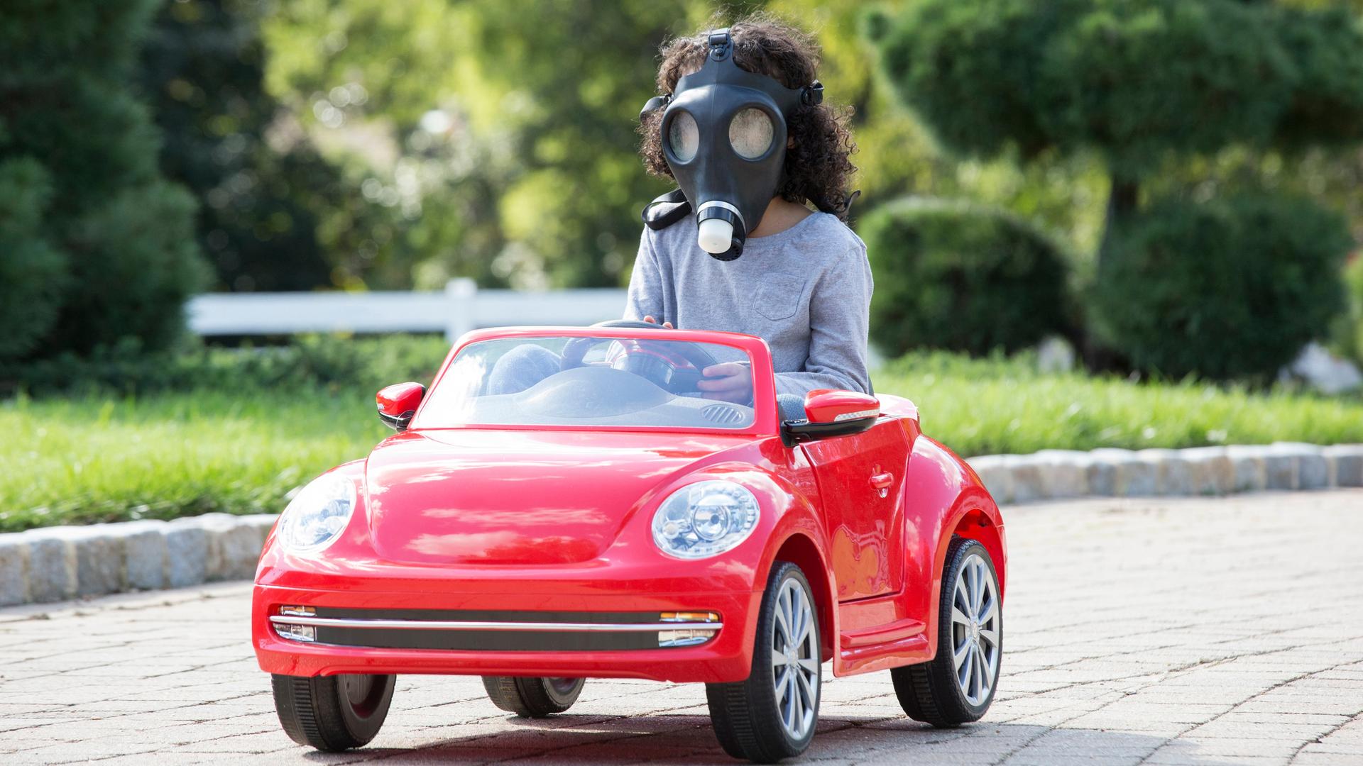 Ein Kind mit einer Gasmaske führt mit einem roten Spielzeugauto.