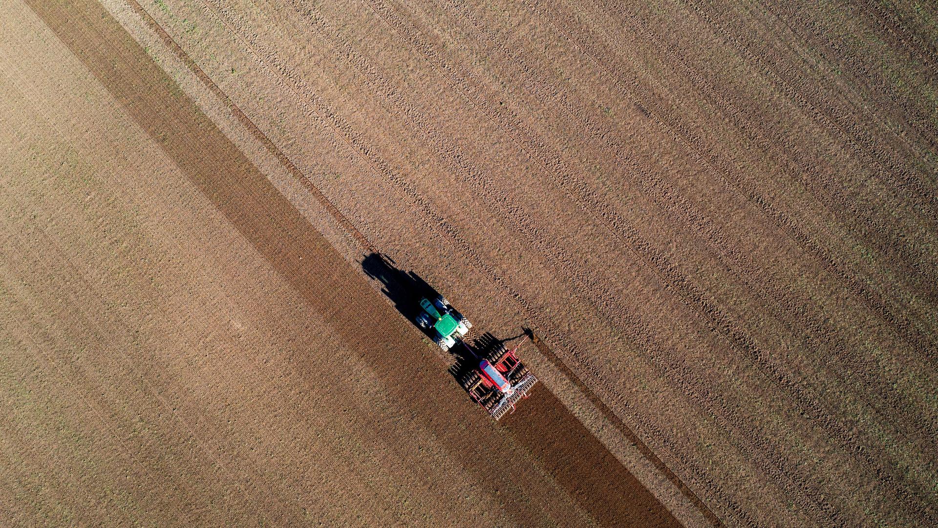 Ein Traktor zieht eine Drillmaschine über einen Acker und bringt Saatgut aus. 