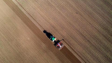 Ein Traktor zieht eine Drillmaschine über einen Acker und bringt Saatgut aus. 