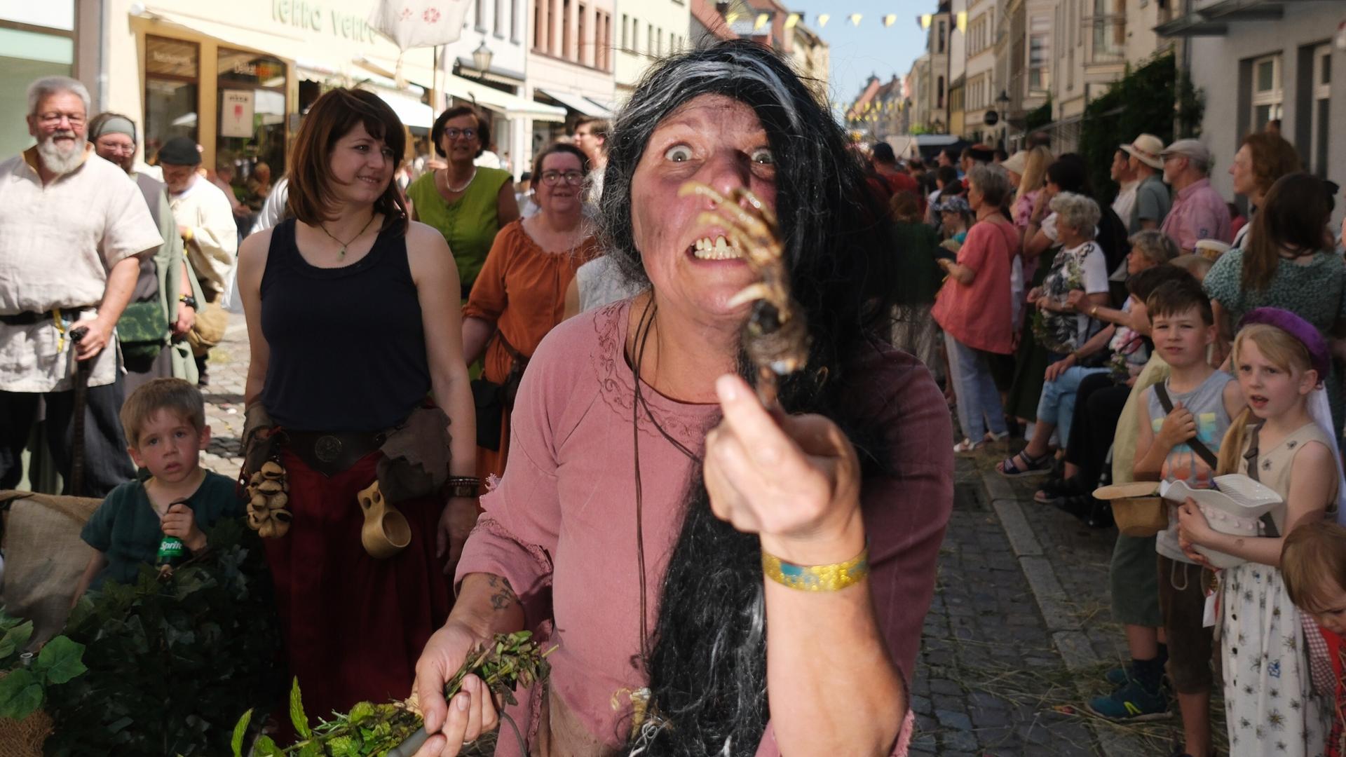Eine Hexendarstellerin ist beim historischen Festumzug des dreitägigen Stadtfestes „Luthers Hochzeit“ zu sehen. Sie zeigt das Skelett einer Tierpfote in die Kamera und ist im Gesicht schmutzig geschminkt. Eine Hexendarstellerin ist beim historischen Festumzug des dreitägigen Stadtfestes „Luthers Hochzeit“ zu sehen. Sie zeigt das Skelett einer Tierpfote in die Kamera und ist im Gesicht schmutzig geschminkt.