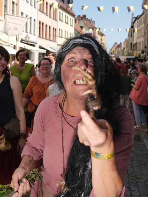Eine Hexendarstellerin ist beim historischen Festumzug des dreitägigen Stadtfestes „Luthers Hochzeit“ zu sehen. Sie zeigt das Skelett einer Tierpfote in die Kamera und ist im Gesicht schmutzig geschminkt.