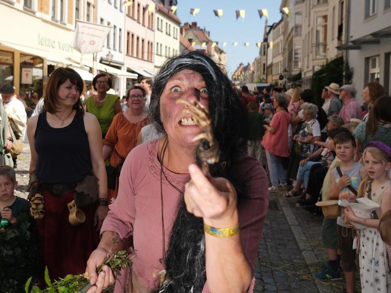 Eine Hexendarstellerin ist beim historischen Festumzug des dreitägigen Stadtfestes „Luthers Hochzeit“ zu sehen. Sie zeigt das Skelett einer Tierpfote in die Kamera und ist im Gesicht schmutzig geschminkt.