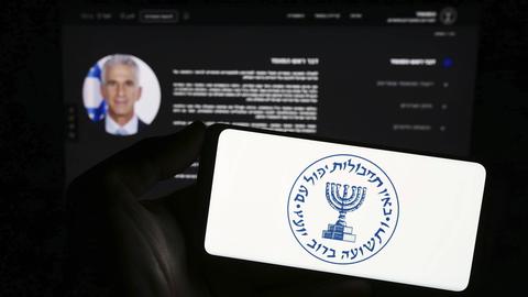 Eine Person hält ein Smartphone mit dem Logo des israelischen Geheimdienstes. 