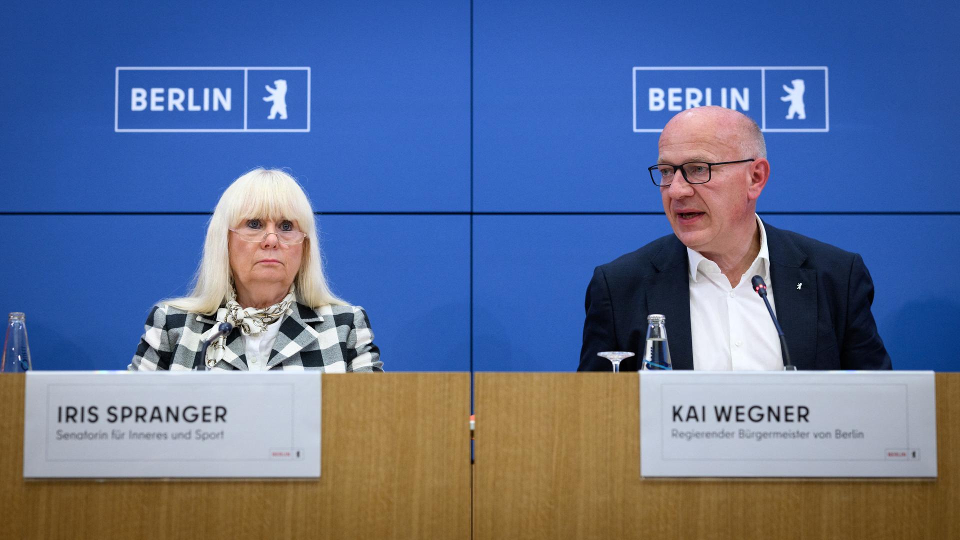 Kai Wegner (r, CDU), Regierender Bürgermeister von Berlin, und Iris Spranger (SPD), Berliner Senatorin für Inneres und Sport, sitzen bei einer Pressekonferenz nebeneinander vor einem blauen Hintergrund.