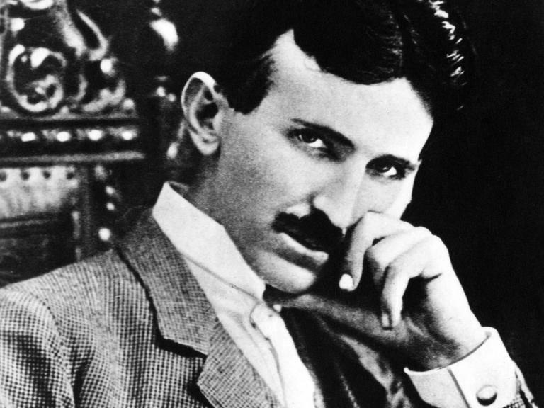  Ingenieur Nikola Tesla. Ein Mann im Anzug mit dunklen kurzen Haaren sitzt auf einem Stuhl und schaut in die Kamera. 