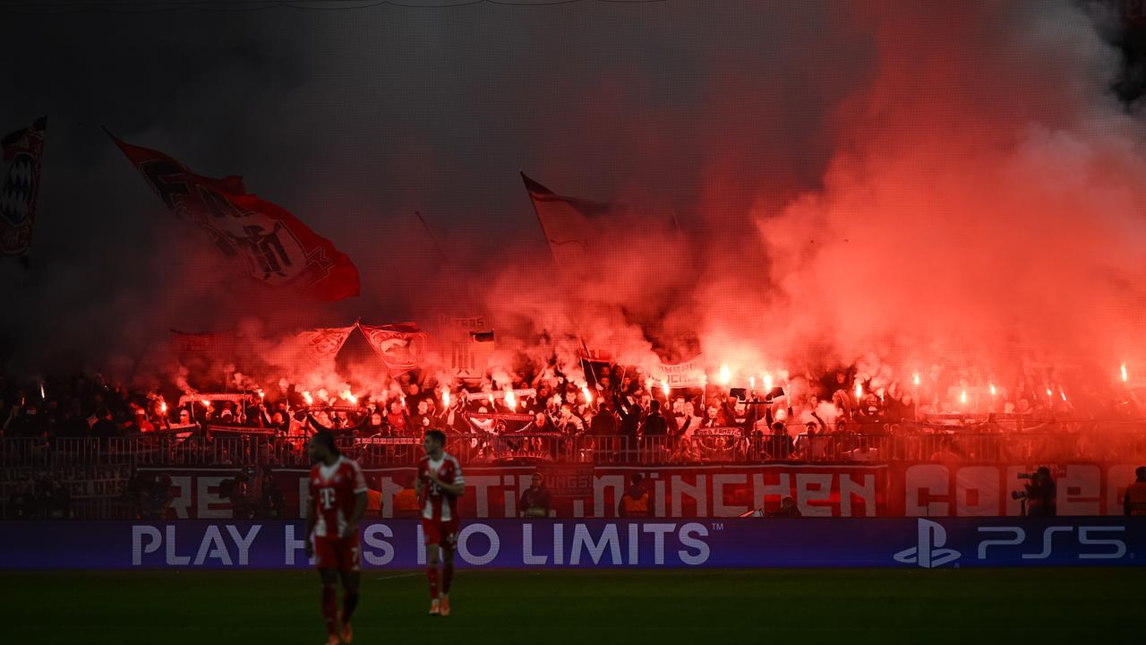 In der Fankurve von Bayern München halten Zuschauer brennende Fackeln in die Luft, es leuchtet rot und qualmt.