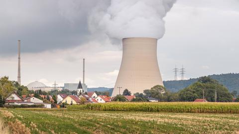 Der dampfende Kühlturm des Kernkraftwerks "Isar 2" in Bayern, im Vordergrund das Dorf Wattenbacherau mit Ziegeldächern und Kirchturm