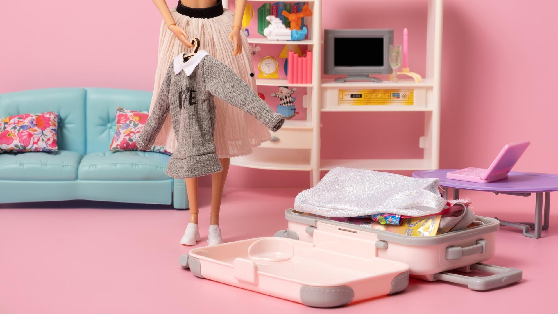 Eine Barbiepuppe packt ihren Koffer in einem rosa Zimmer mit pastellfarbenen Möbeln. Eine Barbiepuppe packt ihren Koffer in einem rosa Zimmer mit pastellfarbenen Möbeln.