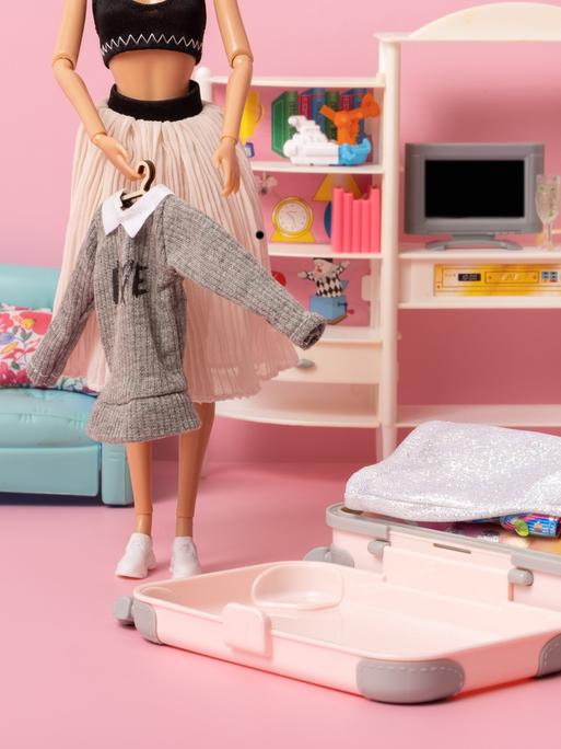 Eine Barbiepuppe packt ihren Koffer in einem rosa Zimmer mit pastellfarbenen Möbeln. Eine Barbiepuppe packt ihren Koffer in einem rosa Zimmer mit pastellfarbenen Möbeln.