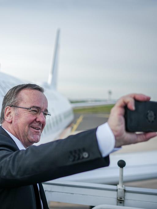 Bundesverteidigungsminister Boris Pistorius fotografiert sich mit seinem Handy selbst auf dem militärischen Teil des Flughafens BER Berlin-Brandenburg vor dem Airbus der Flugbereitschaft.