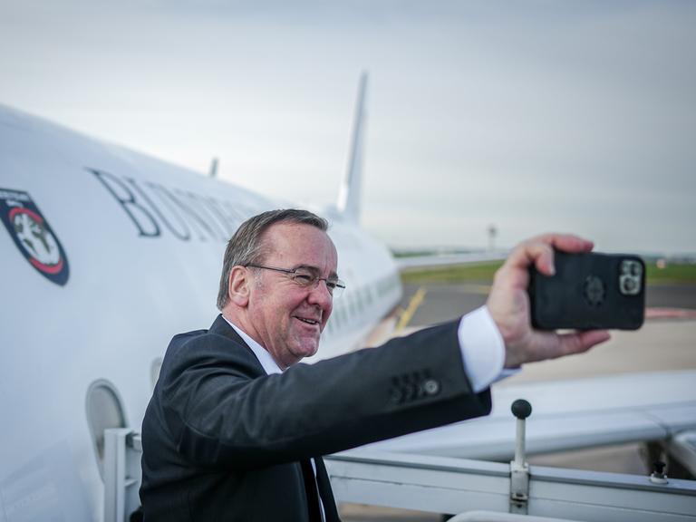 Bundesverteidigungsminister Boris Pistorius fotografiert sich mit seinem Handy selbst auf dem militärischen Teil des Flughafens BER Berlin-Brandenburg vor dem Airbus der Flugbereitschaft.