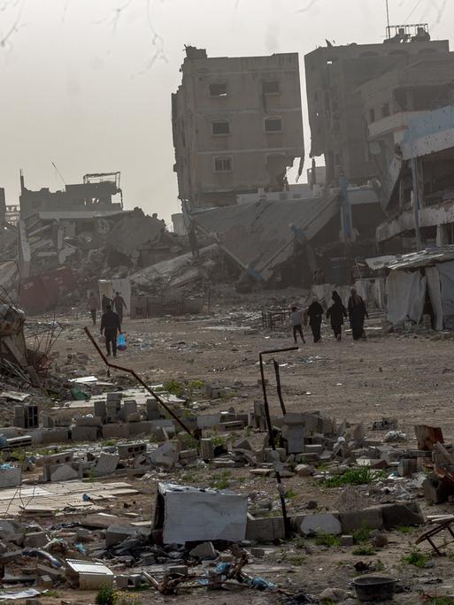 Palästinenser laufen durch eine zerstörte Umgebung. 