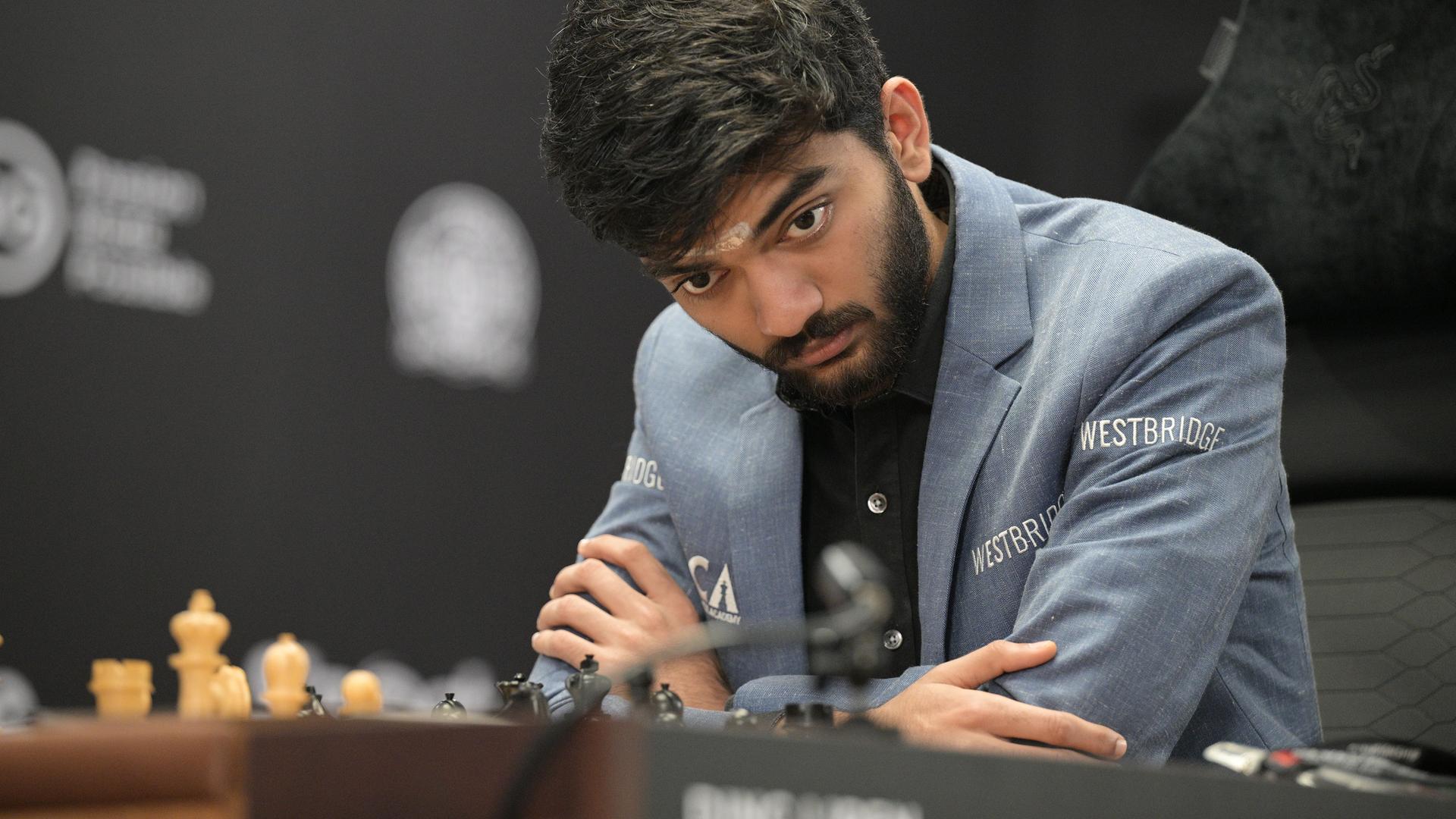Der indische Schachweltmeister Dommaraju Gukesh blickt konzentriert auf Schachbrett. 
