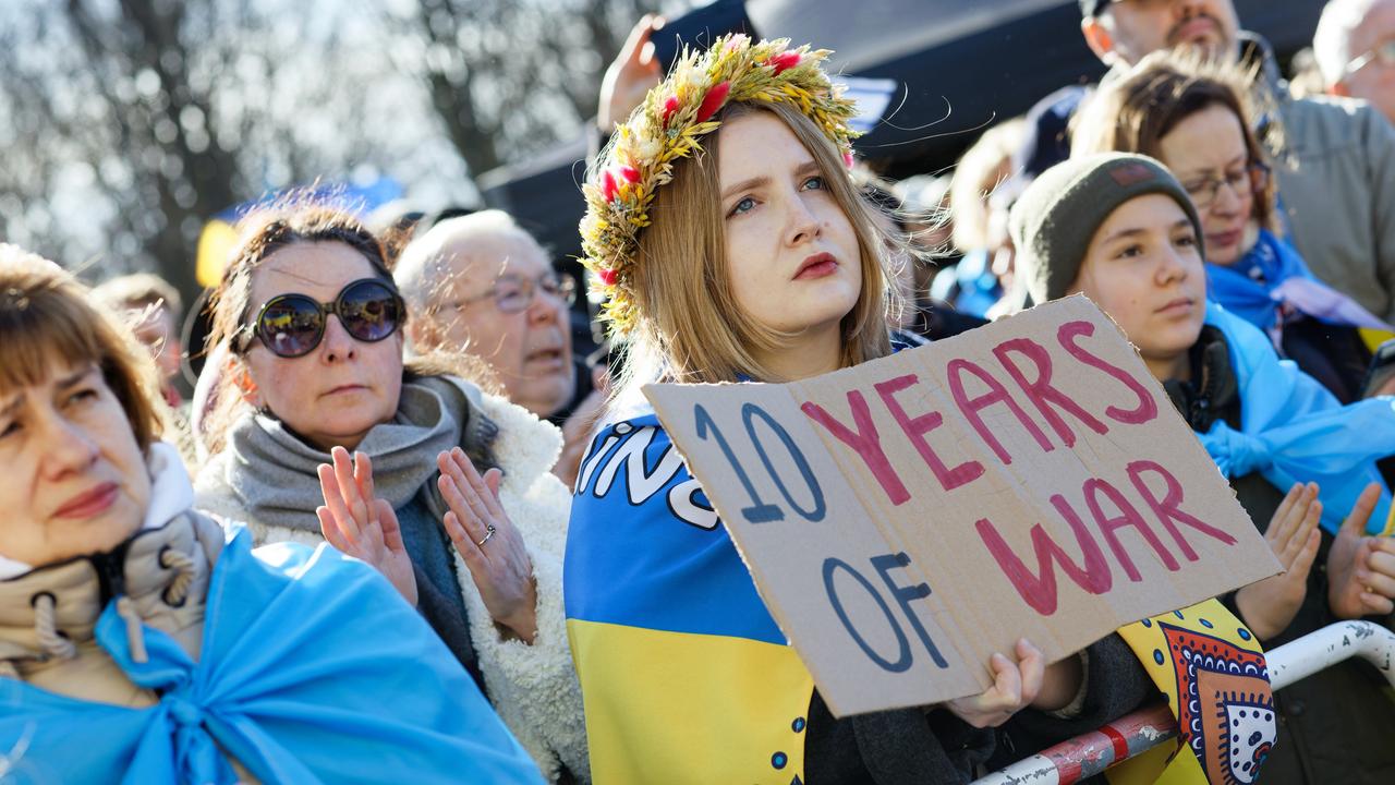 Eine Frau mit einem Blumenkranz auf dem Kopf hält auf einer pro-ukrainischen Demonstration ein Pappschild mit der Aufschrift: 10 Years of War. 