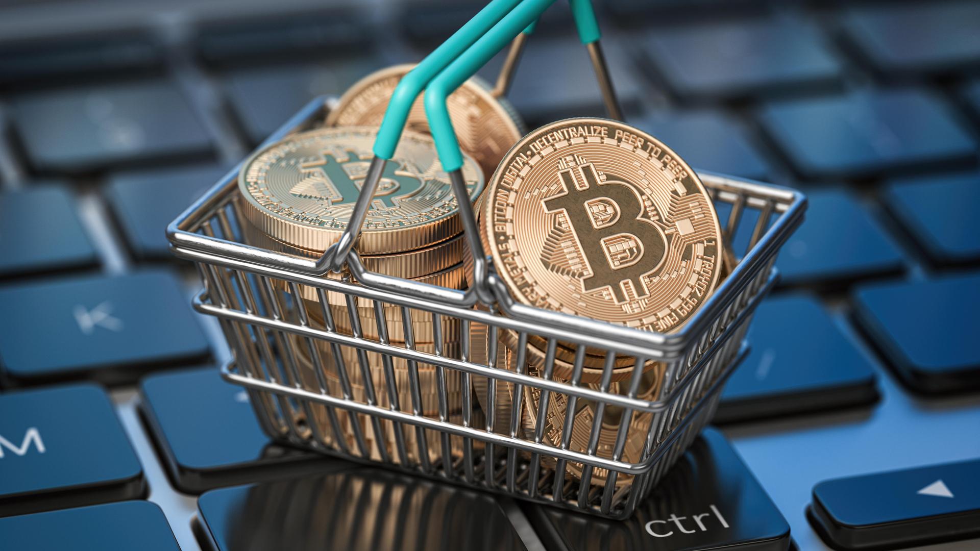 Bitcoin-Münzen liegen in einem Mini-Einkaufskorb, der auf einer Computertastatur steht.