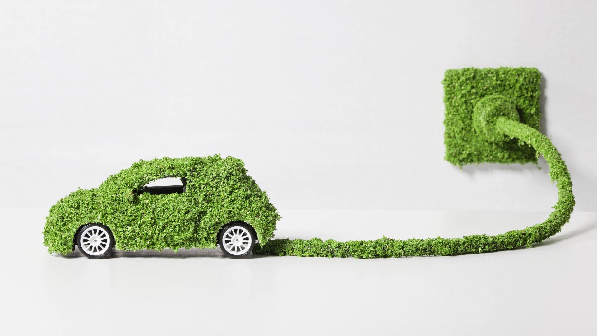 Mit Moos überwachsenes Elektroauto, das an eine Steckdose angeschlossen ist. Mit Moos überwachsenes Elektroauto, das an eine Steckdose angeschlossen ist.