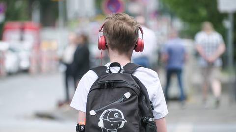 Ein Junge ist von hinten zu sehen. Er trägt Kopfhörer und einen schwarzen Rucksack, auf dem ebenfalls ein Junge mit Kopfhörer zu sehen ist. 