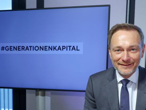 Ein Mann mit hellen Haaren schaut in die Kamera und lacht. Er trägt einen Anzug. Hinter ihm ist ein Monitor auf dem "Generationenkapital" steht. Ees ist Christian Lindner (FDP). Der Bundesfinanzminister nimmt an einer Veranstaltung in Frankfurt teil.