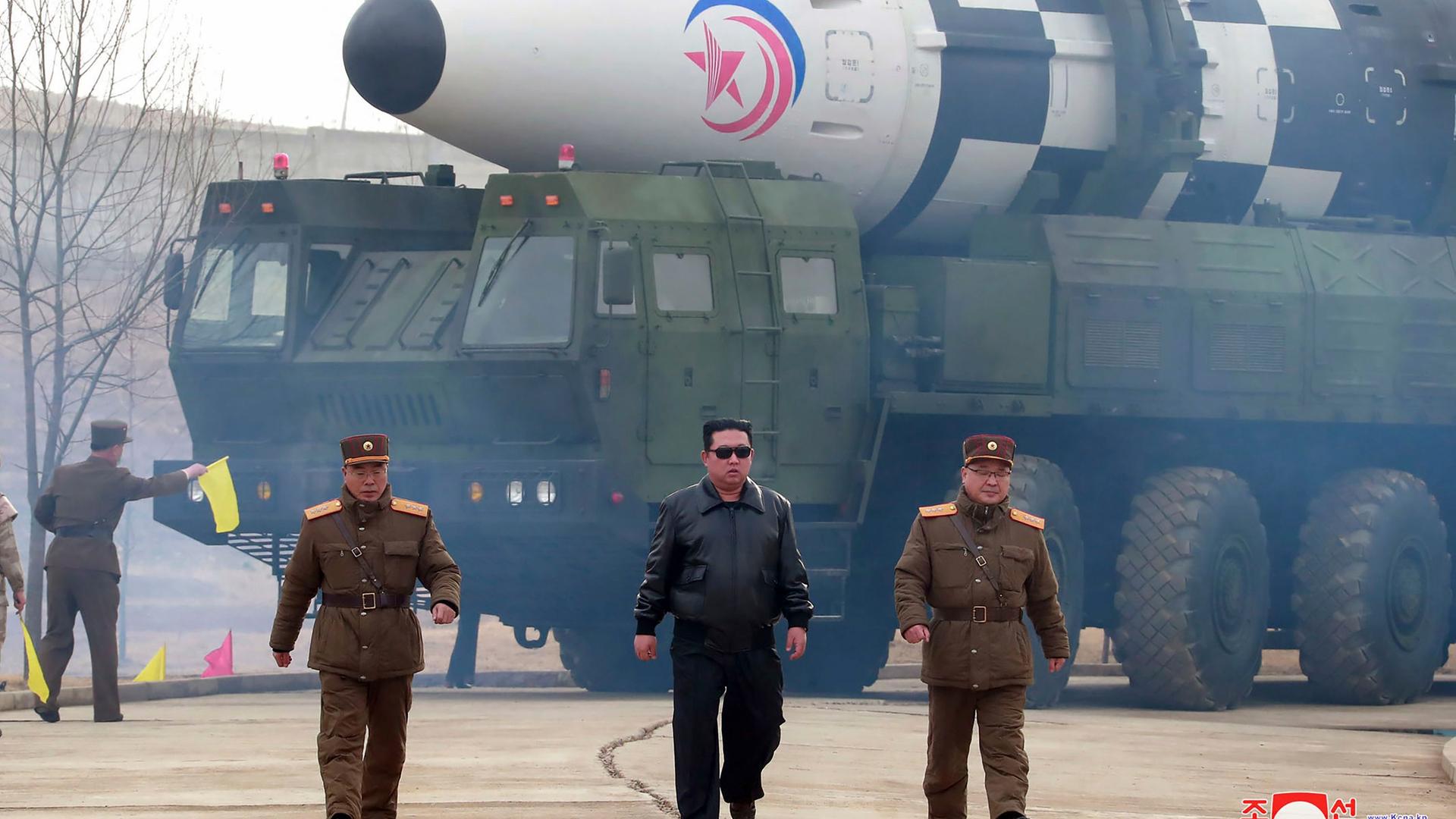 Der nordkoreanische Machthaber Kim Jong-un gemeinsam mit zwei Mitgliedern des Militärs - im Hintergrund ist eine Langstreckenrakete zu sehen.