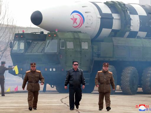 Der nordkoreanische Machthaber Kim Jong-un gemeinsam mit zwei Mitgliedern des Militärs - im Hintergrund ist eine Langstreckenrakete zu sehen.