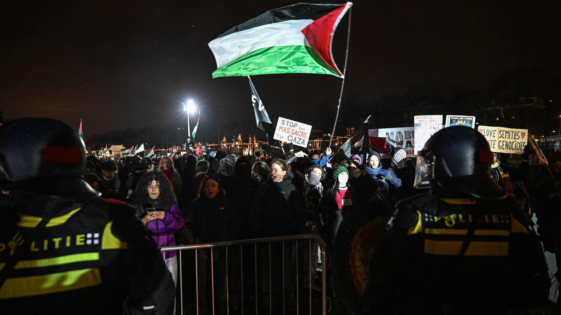 Demonstranten mit palästinensischen Flaggen und Transparenten bei Nacht; davor stehen Polizisten in Einsatzmontur Demonstranten mit palästinensischen Flaggen und Transparenten bei Nacht; davor stehen Polizisten in Einsatzmontur