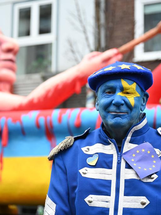 Jacques Tilly steht im Februar 2023 vor einem Karnevalswagen, der den russischen Präsidenten Putin zeigt. Dieser nimmt ein Blutbad in einer Badewanne in den Farben der Ukraine. 
