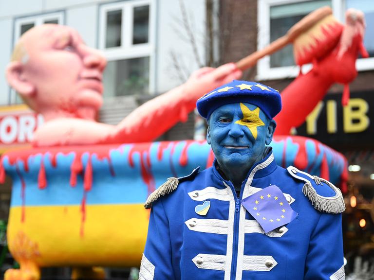 Jacques Tilly steht im Februar 2023 vor einem Karnevalswagen, der den russischen Präsidenten Putin zeigt. Dieser nimmt ein Blutbad in einer Badewanne in den Farben der Ukraine. 