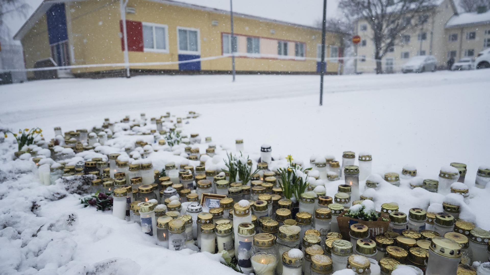 Kerzen und Blumen stehen vor der Schule in Vantaa im Schnee.
