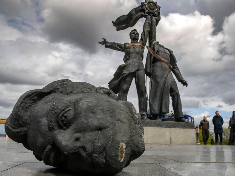 Zwei Statuen halten einen Sowjetstern in ihren Händen. Der rechten fehlt der Kopf, er liegt vor ihnen auf dem Boden.