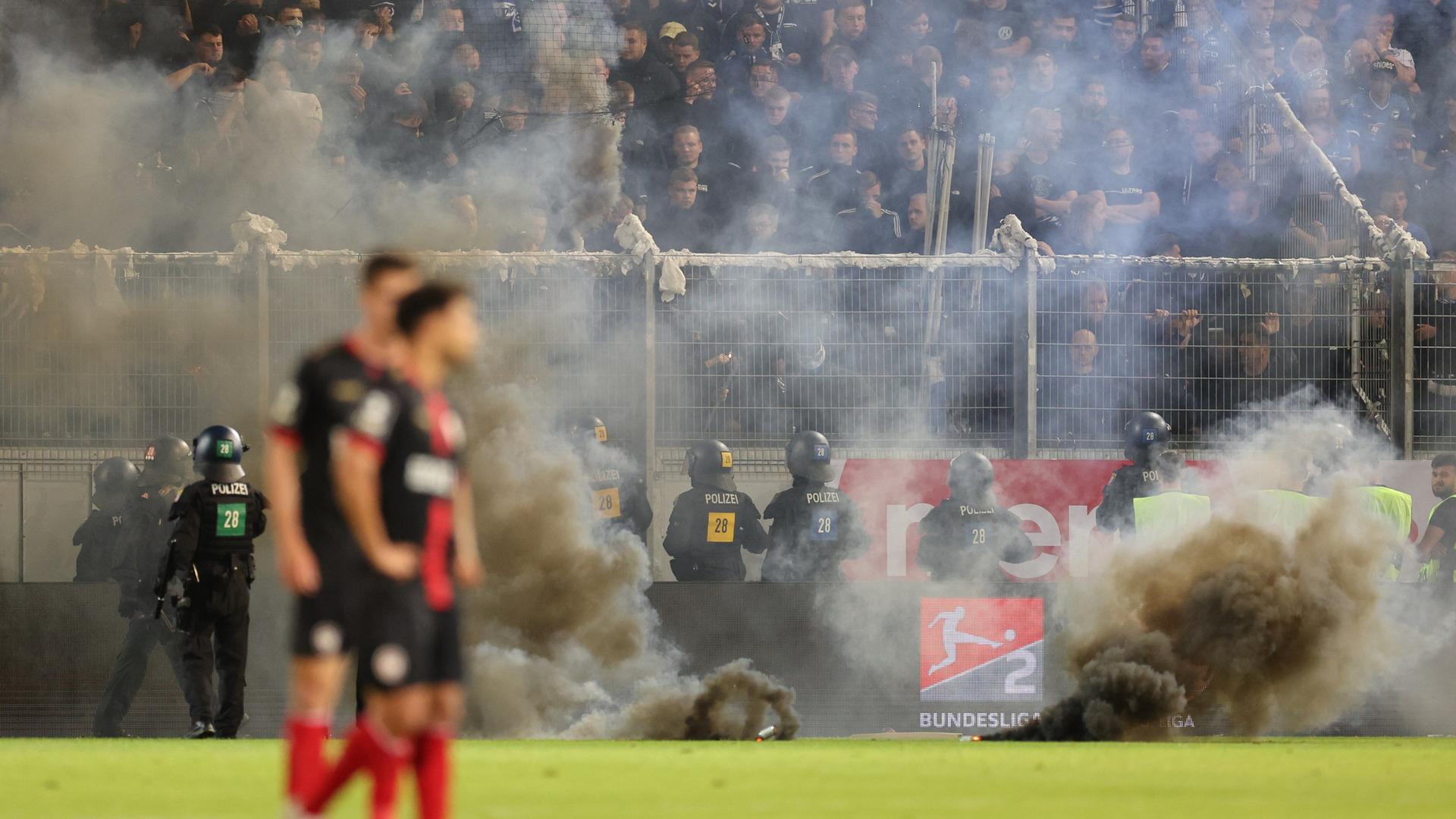 In der BRITA-Arena in Wiesbaden wird Pyrotechnik gezündet. Polizeieinsatzkräfte stehen vor dem Block der Bielefelder Fans.