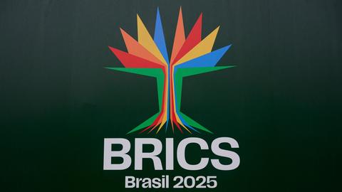 Zu sehen ist das Symbol des diesjährigen Gipfels: ein stilisierter Baum aus hellgrünen, -blauen, -gelben, -roten und -orangefarbenen, gewinkelten Streifen. Darunter steht BRICS und Brasil 2025 auf dunkelgrünem Grund.