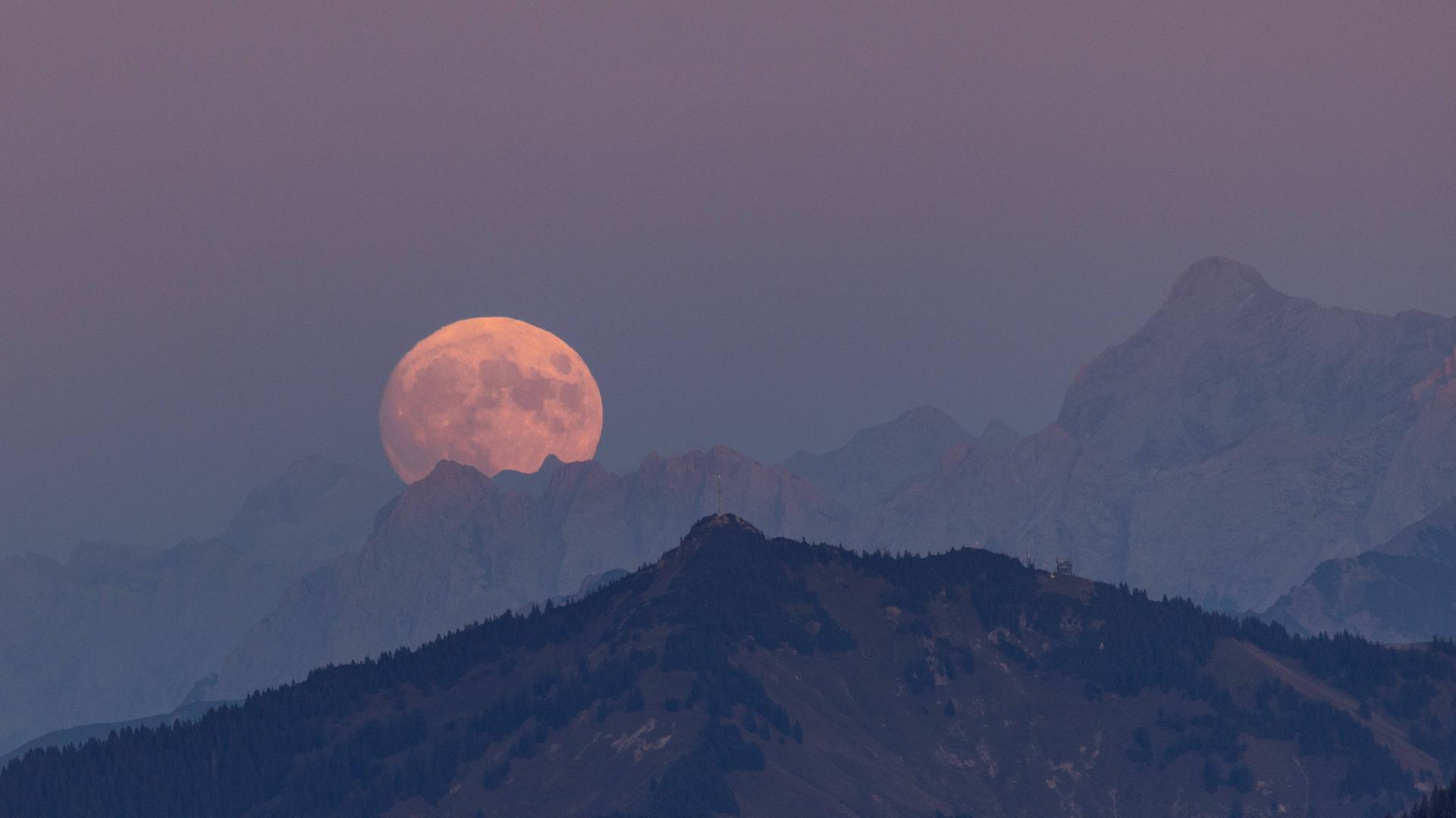 Ein Vollmond über einer Bergkuppe in den Alpen.