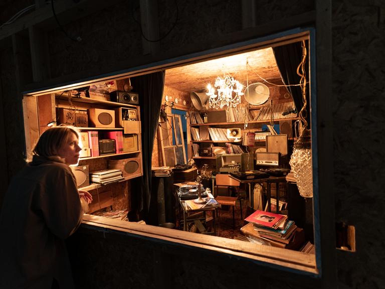 Eine Frau schaut durch ein Schaufenster in einen kleinen mit Schallplatten und Archivalien vollgestopften Raum