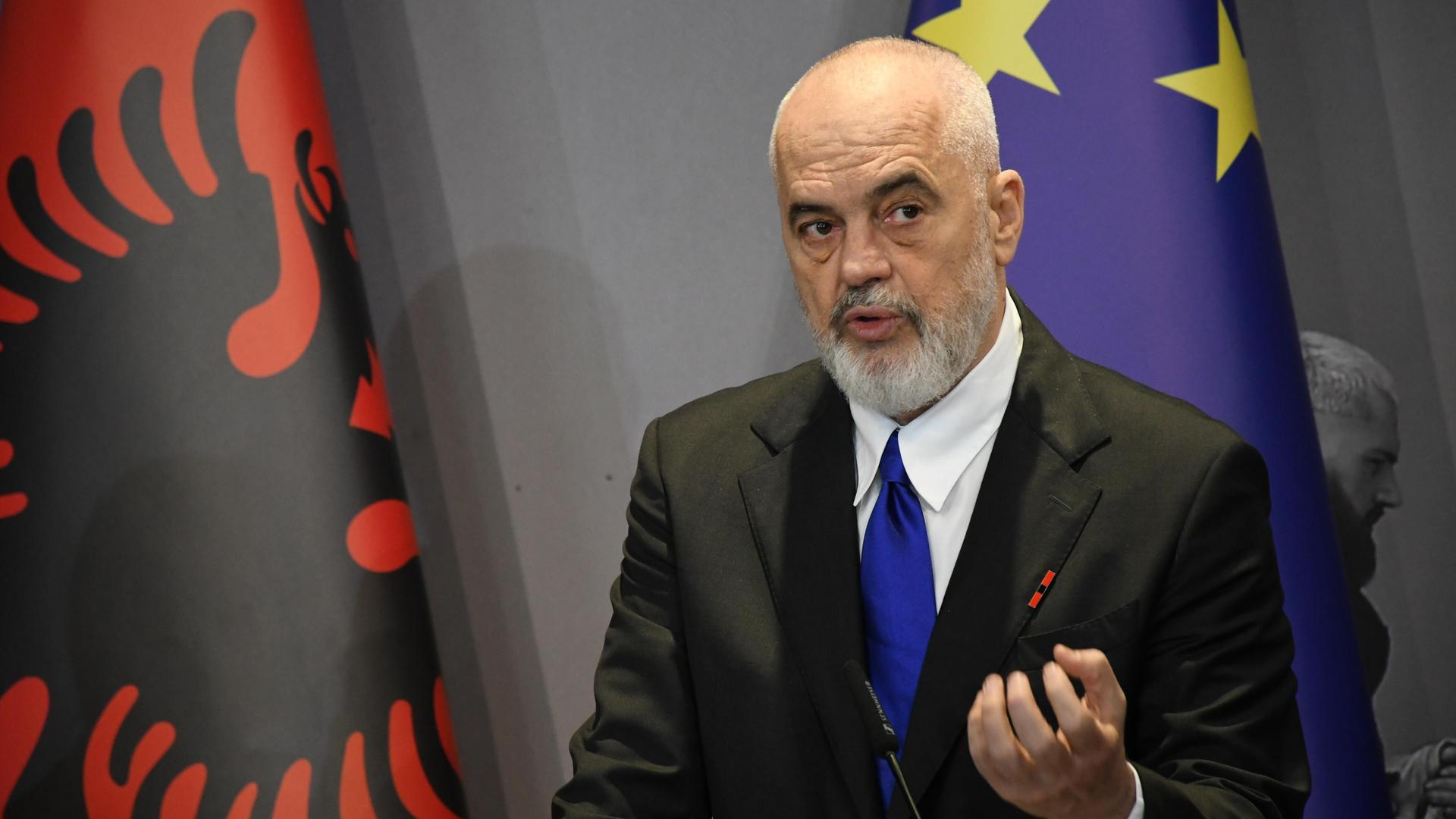 Edi Rama steht vor der albanischen und der europäischen Flagge und spricht.
