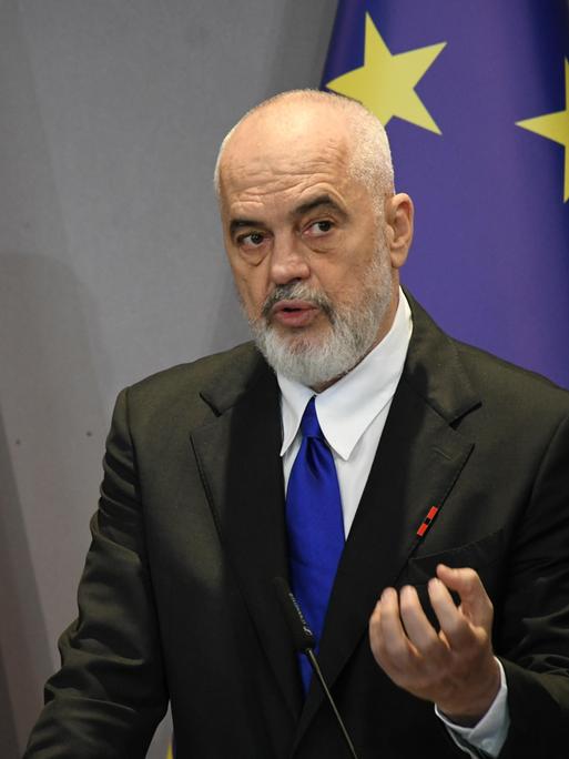 Edi Rama steht vor der albanischen und der europäischen Flagge und spricht.