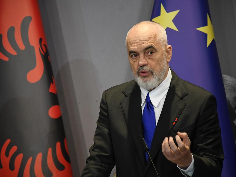 Edi Rama steht vor der albanischen und der europäischen Flagge und spricht.