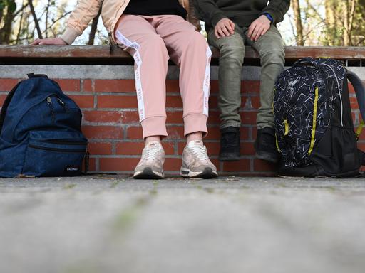 Eine Schülerin sitzt in einer Jogginghose auf demÂ Schulhof einer Schule.