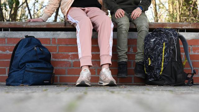 Eine Schülerin sitzt in einer Jogginghose auf dem Schulhof einer Schule. Abgebildet sind nur die Beine. 