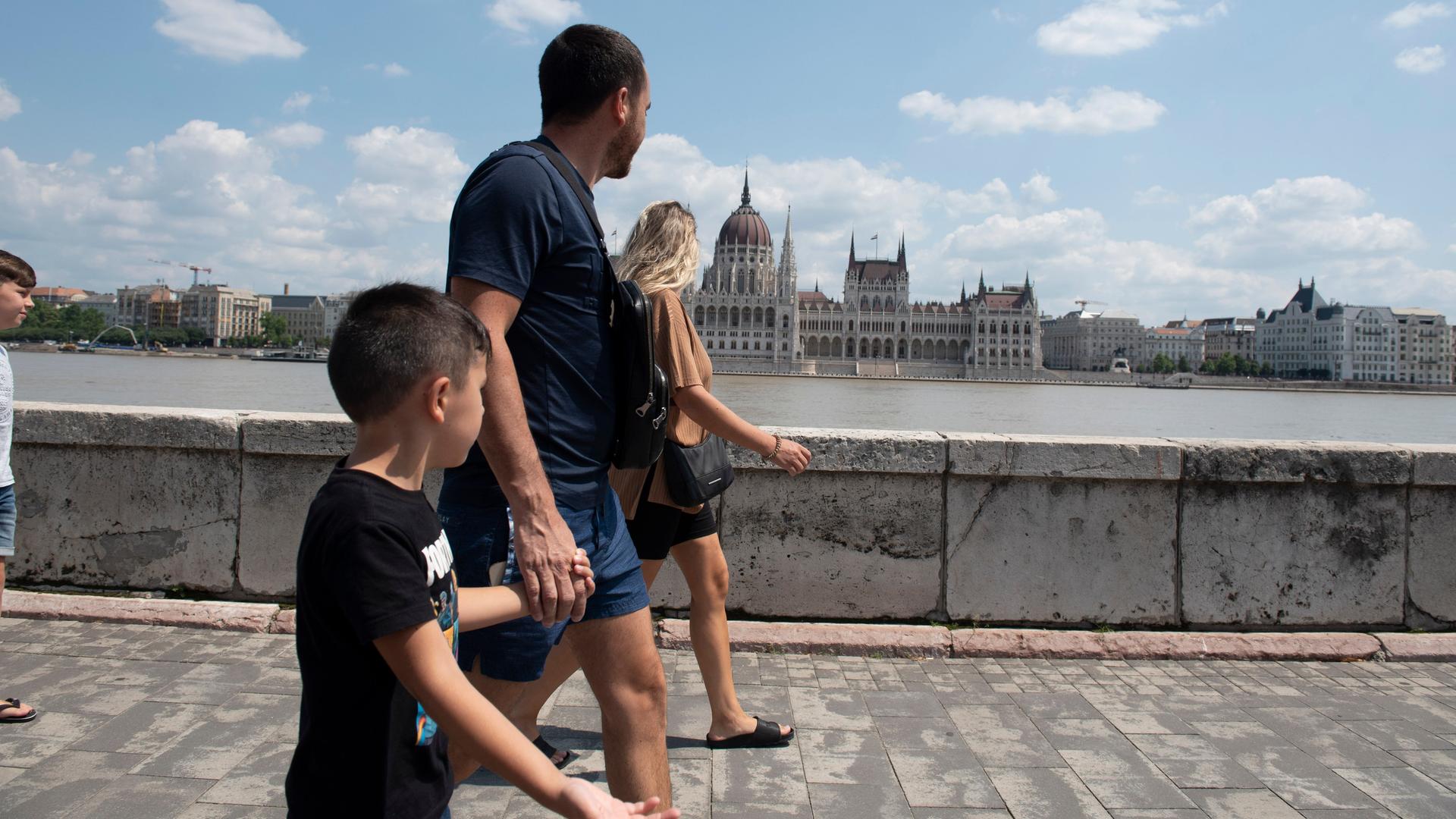 Eine Familie läuft am Ufer der Donau in Budapest entlang, auf der anderen Flussseite ist das Parlamentsgebäude zu sehen