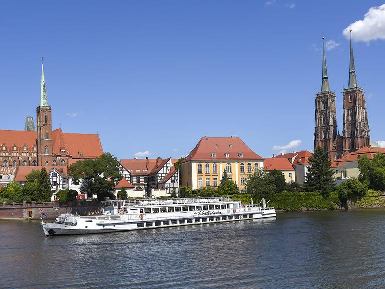Panorama der Stadt Breslau mit der St. John-Kathedrale im Hintergrund, im Vordergrund ein Schiff auf der Oder.