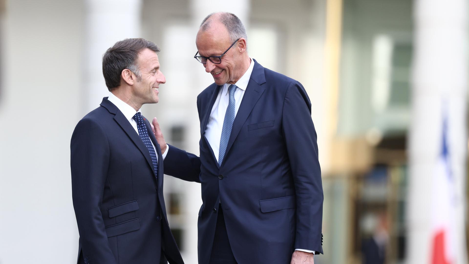 Bundeskanzler Merz empfängt den französischen Präsidenten Macron auf Schloss Bensberg in Nordrhein-Westfalen. Beide tragen dunkelblaue Anzüge und lächeln sich freundlich an. Bundeskanzler Merz empfängt den französischen Präsidenten Macron auf Schloss Bensberg in Nordrhein-Westfalen. Beide tragen dunkelblaue Anzüge und lächeln sich freundlich an.