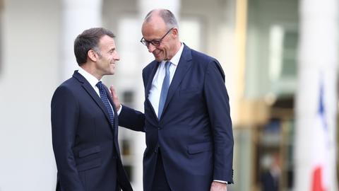 Bundeskanzler Merz empfängt den französischen Präsidenten Macron auf Schloss Bensberg in Nordrhein-Westfalen. Beide tragen dunkelblaue Anzüge und lächeln sich freundlich an.