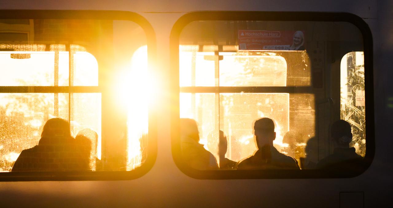 Fahrgäste sitzen bei Sonnenaufgang in einer Stadtbahn.