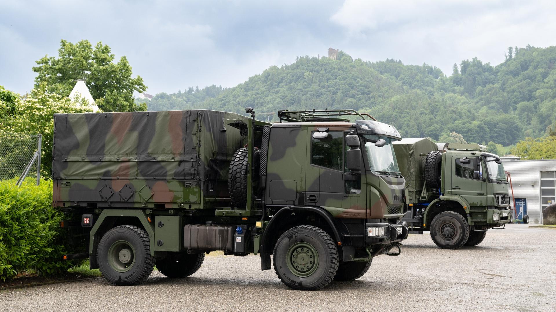 Die beiden in Tarnfarben lackierten Lkw stehen nebeneinander auf einem Parkplatz. Im Hintergrund Wald und Hecken. Die beiden in Tarnfarben lackierten Lkw stehen nebeneinander auf einem Parkplatz. Im Hintergrund Wald und Hecken.