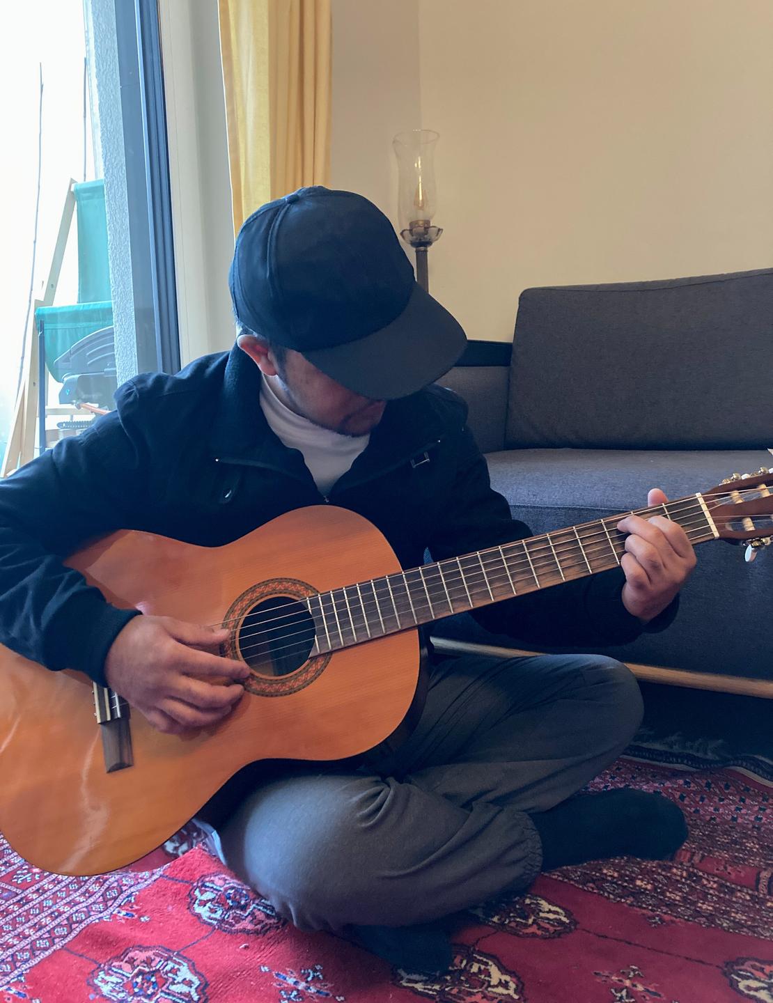 Romy Padilla. Ein junger Mann sitzt in einem Zimmer und spielt Gitarre. 