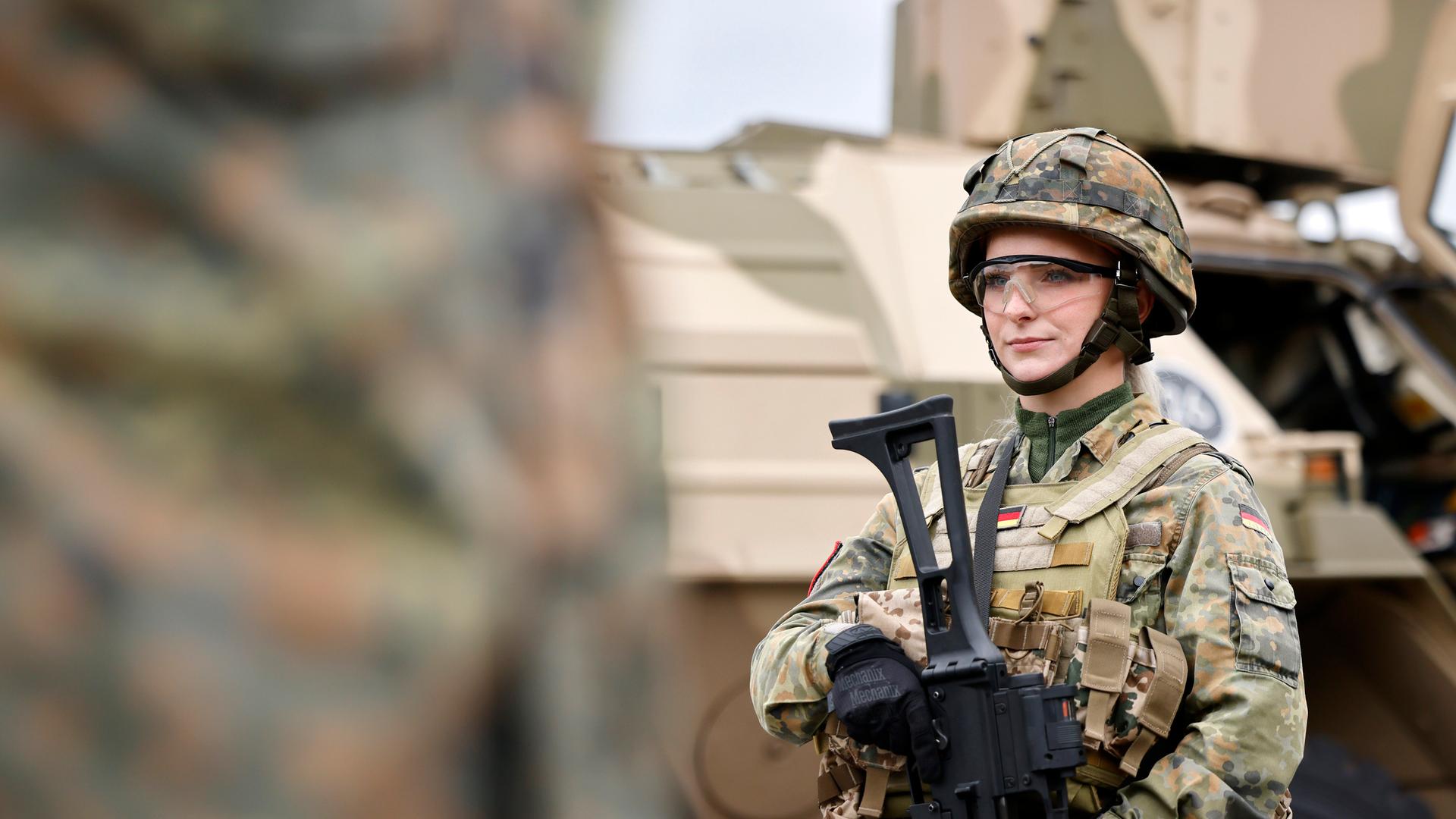 Eine Bundeswehr-Soldatin in Tarnanzug mit G36 Gewehr steht vor einem Militärfahrzeug Eine Bundeswehr-Soldatin in Tarnanzug mit G36 Gewehr steht vor einem Militärfahrzeug
