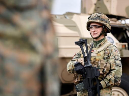 Eine Bundeswehr-Soldatin in Tarnanzug mit G36 Gewehr steht vor einem Militärfahrzeug
